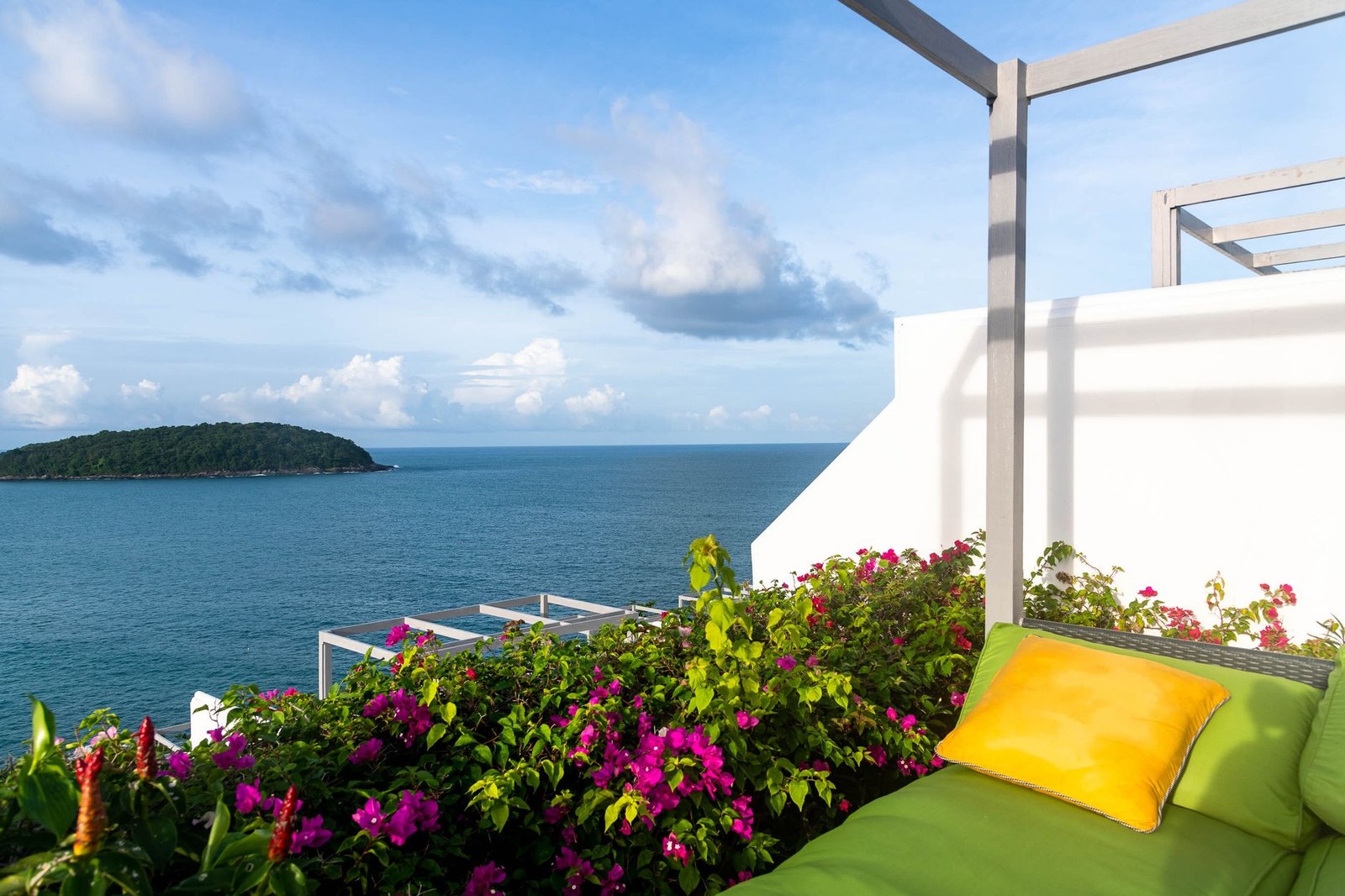 Terraza de hotel sobre el mar con daybed de exterior de cojines verdes bajo pérgola blanca, mobiliario contract fabricado en China