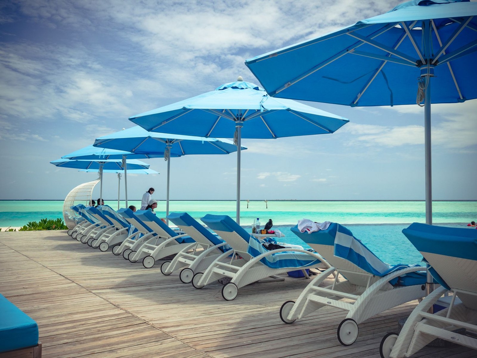 Bains de soleil blancs, parasols bleus et lits de jour sur une plage de resort en bord de lagon turquoise