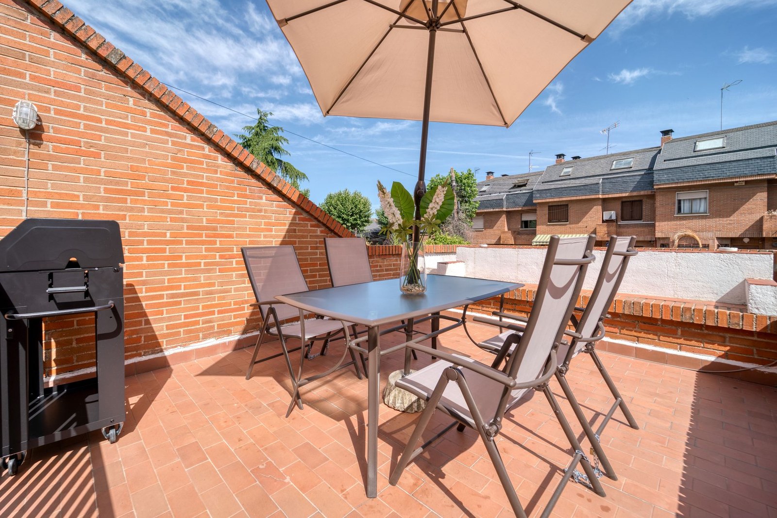 Mesa de terraza de aluminio con cuatro sillas de textileno y sombrilla central en una terraza urbana, mobiliario de hostelería fabricado en China