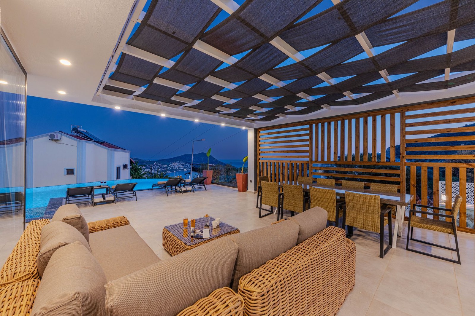 Terraza cubierta al atardecer con sofá modular de ratán sintético, mesa baja y zona de comedor, conjunto de sofás de exterior para hotel
