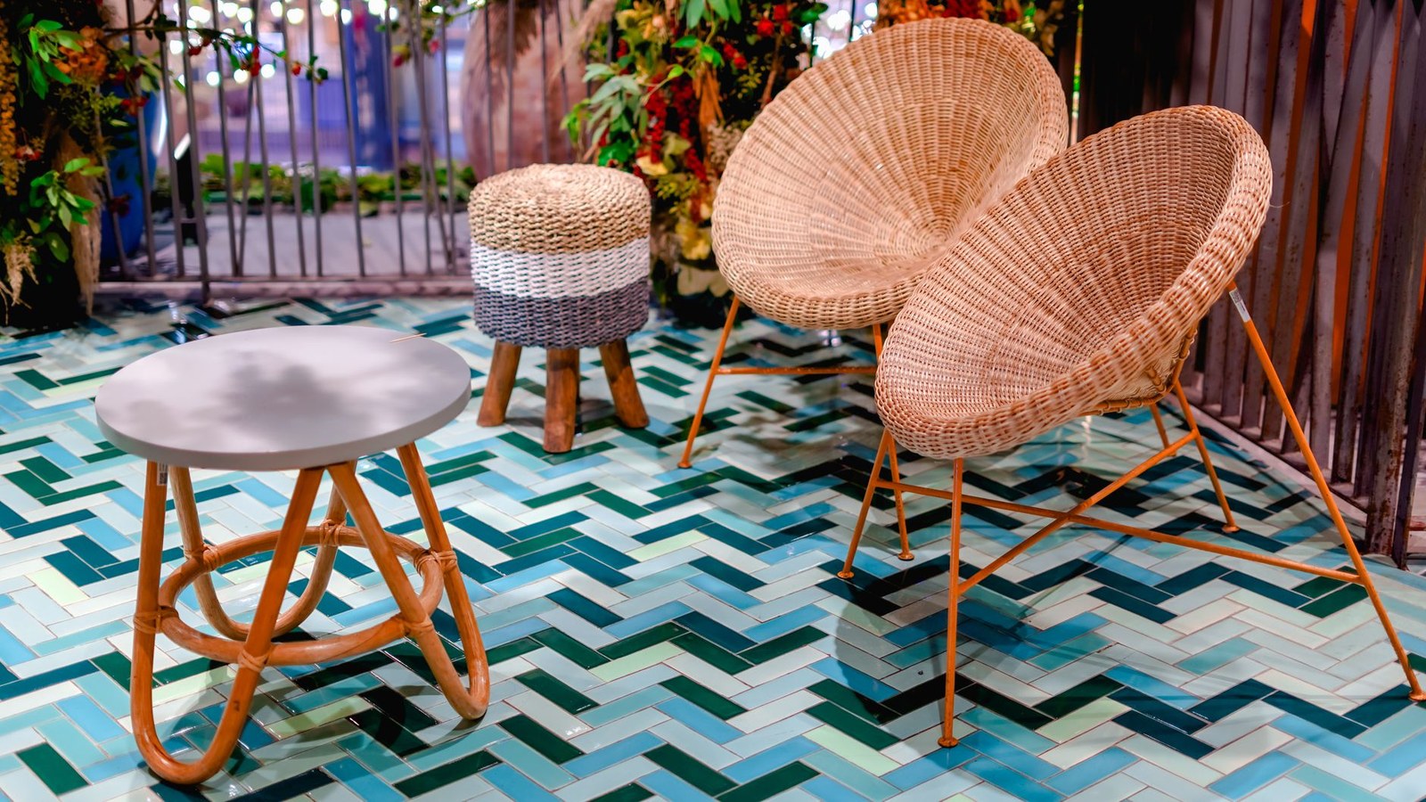 Detalle de asiento y puf de ratán sintético trenzado con patas metálicas y mesa auxiliar en una terraza, tejido HDPE para muebles de exterior