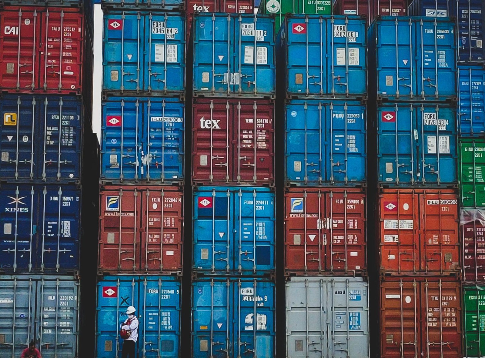 Contenedores de carga apilados en un patio logístico con operarios, exportación de sofás de exterior desde China